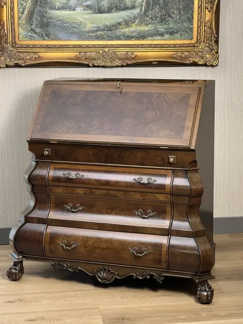 Bureau closed, standing against a wall below a framed painting.