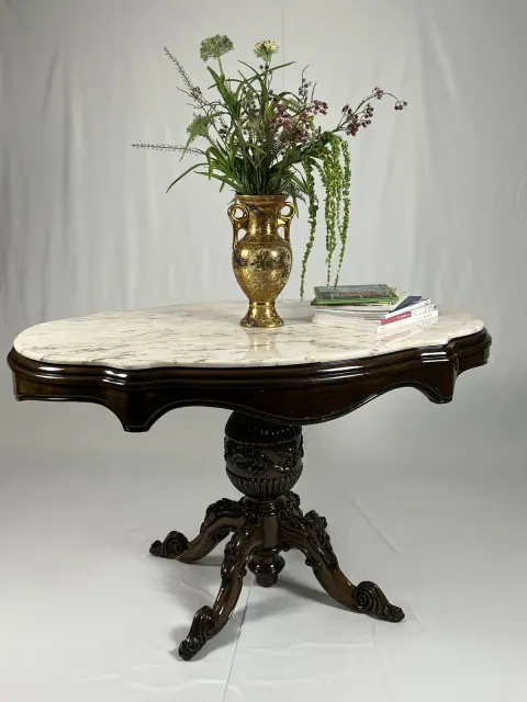 Marble-top table on a carved pedestal, with a vase and books on it.