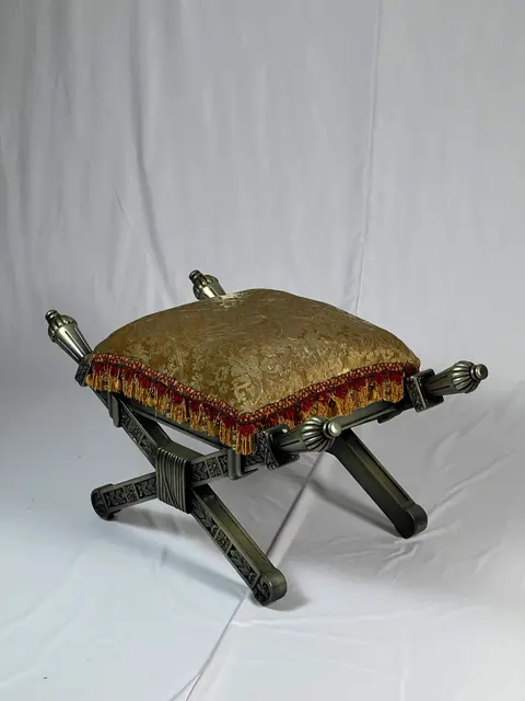 X-frame stool with a gold damask cushion and red fringe.